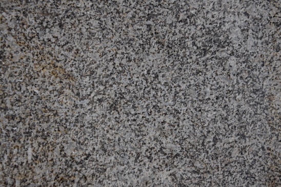 A close-up of a textured granite surface featuring a mix of gray, black, and subtle brown speckles.
