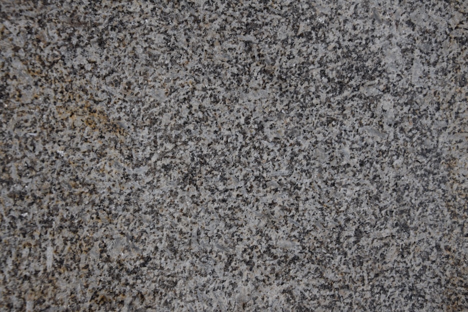 A close-up of a textured granite surface featuring a mix of gray, black, and subtle brown speckles.