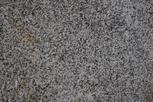 A close-up of a textured granite surface featuring a mix of gray, black, and subtle brown speckles.