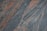 A textured granite surface with swirling patterns of gray and reddish-orange. The composition creates a dynamic and natural appearance with variations in color and texture across the stone.