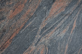 A textured granite surface with swirling patterns of gray and reddish-orange. The composition creates a dynamic and natural appearance with variations in color and texture across the stone.