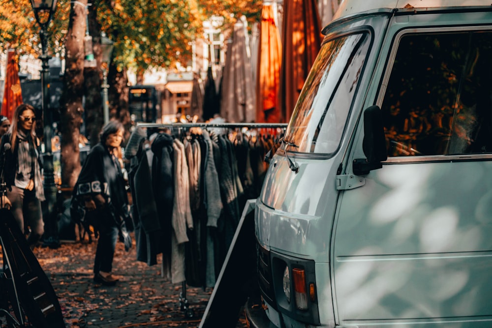 parked white vehicle beside hanged coats on rack near two women