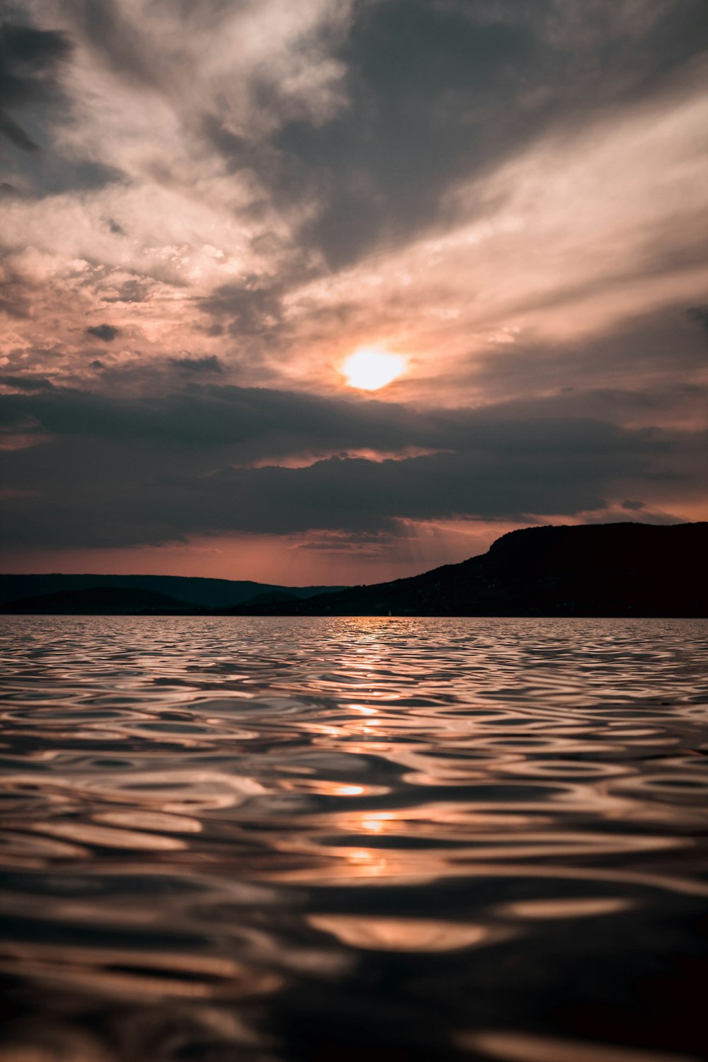 calm sea with silhouette mountain range under dramatic clouds during sunset