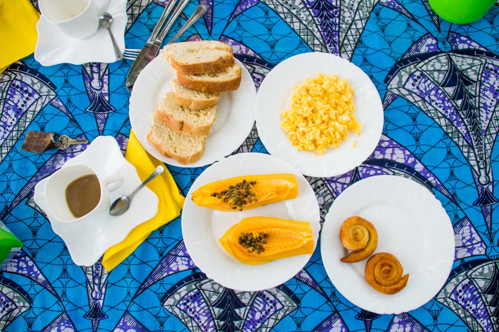 sliced papaya fruits, scramble egg, loaves of bread on white ceramic plates