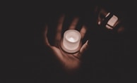 Close-up of hands gently holding a small, glowing candle during twilight.