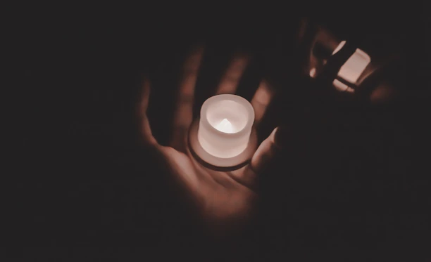 A gentle hand holding a small paw-shaped urn surrounded by soft candlelight.