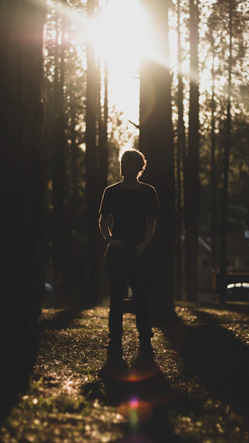 A moody, cinematic portrait of a man standing at dawn in a forest, golden light trails swirling around him.