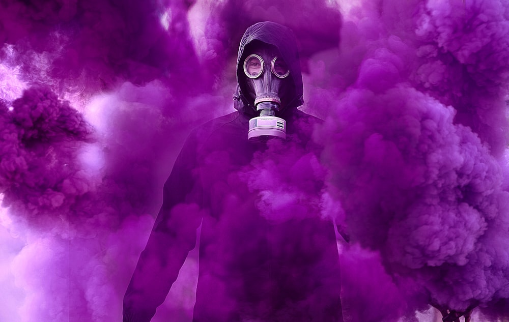 person in black gas mask under purple fog