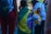 A child draped in a Brazilian flag stands among a group of people. One person is holding a yellow bag with a stuffed bear attached. People are dressed casually, and the scene appears to be outdoors during the day.