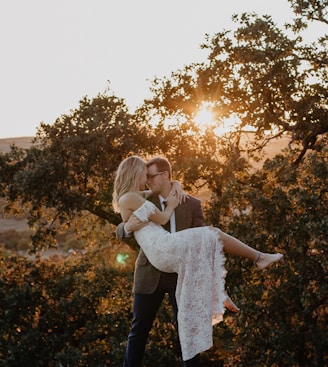 man carrying woman wearing white dress during sunrise