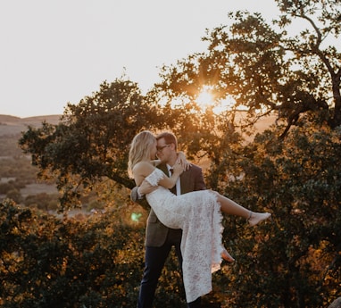 man carrying woman wearing white dress during sunrise