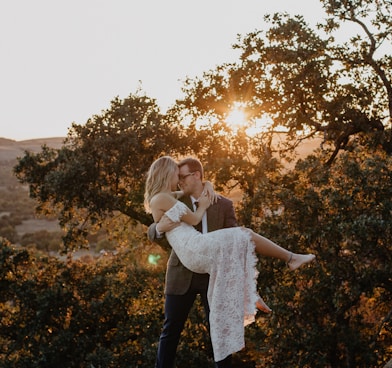 man carrying woman wearing white dress during sunrise