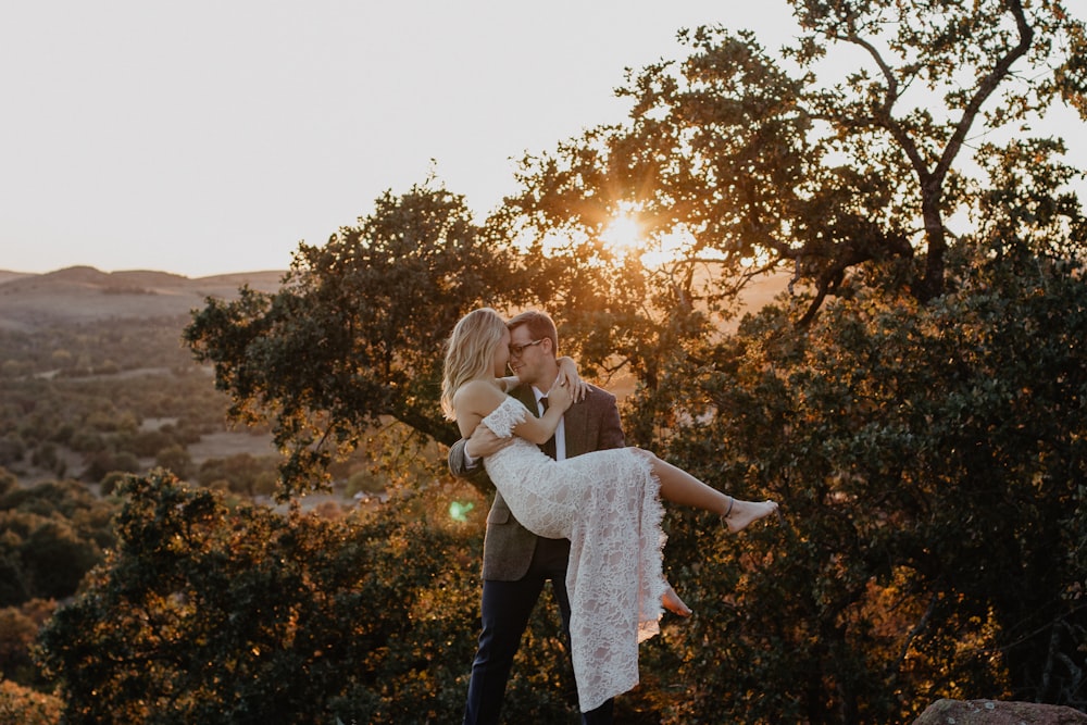 man carrying woman wearing white dress during sunrise