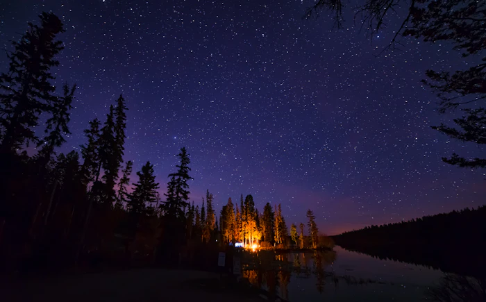 A small campfire by a lake under a starry sky