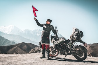 man holding red flag standing beside black sports bike during daytime