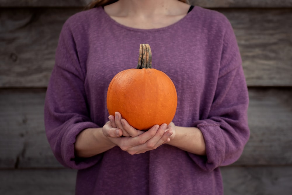 woman in purple crew-neck long-sleeved shirt holding orange pumpkin