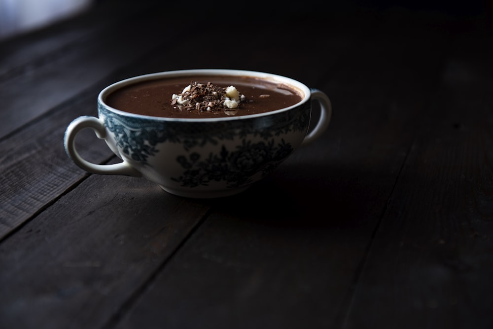 blue and white ceramic teacup with liquid on brown surface