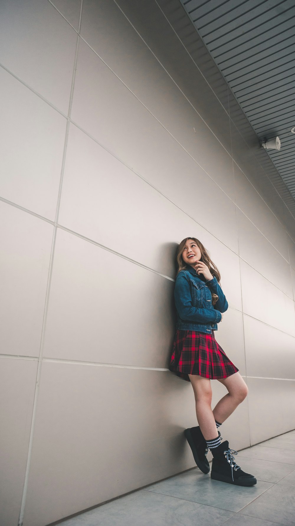girl in blue jacket and red and black mini skirt leaning on wall