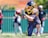A football player wearing a helmet and a sports uniform is on one knee, intently focusing on catching a football. The player is adorned with arm tattoos and wears a jersey with the number 33. In the background, other individuals can be seen standing near a green fence, out of focus.