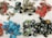 A collection of colorful handmade earrings and rings spread out on a white fabric background. The earrings are in various shapes and colors, including vibrant reds, blues, greens, and gold. Some earrings feature intricate patterns and details. A number of thick, dark green rings are also present.