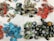 A collection of colorful handmade earrings and rings spread out on a white fabric background. The earrings are in various shapes and colors, including vibrant reds, blues, greens, and gold. Some earrings feature intricate patterns and details. A number of thick, dark green rings are also present.