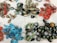 A collection of colorful handmade earrings and rings spread out on a white fabric background. The earrings are in various shapes and colors, including vibrant reds, blues, greens, and gold. Some earrings feature intricate patterns and details. A number of thick, dark green rings are also present.