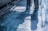 The image features two individuals with only their lower bodies visible. They are standing on a shiny, polished stone floor with visible reflections and shadows. There are cleaning supplies, including a mop and a bottle, placed against the wall on the left side of the image.