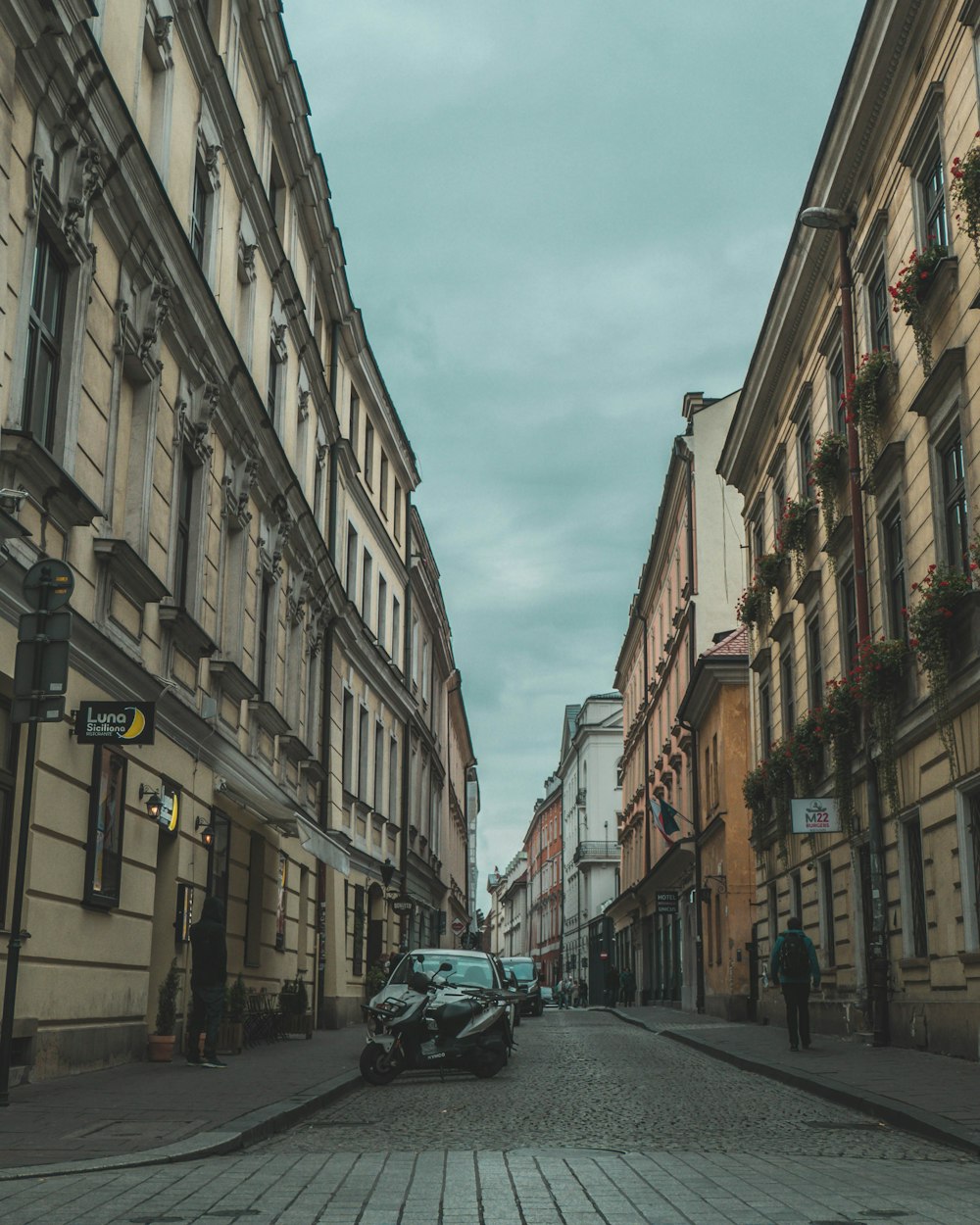 person walking on pavement near vehicles between buildings