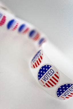 A roll of circular stickers featuring the text 'I Voted' with a design that incorporates elements of the American flag in red, white, and blue colors. The stickers are arranged in a curved manner, indicating that they are part of a continuous roll.