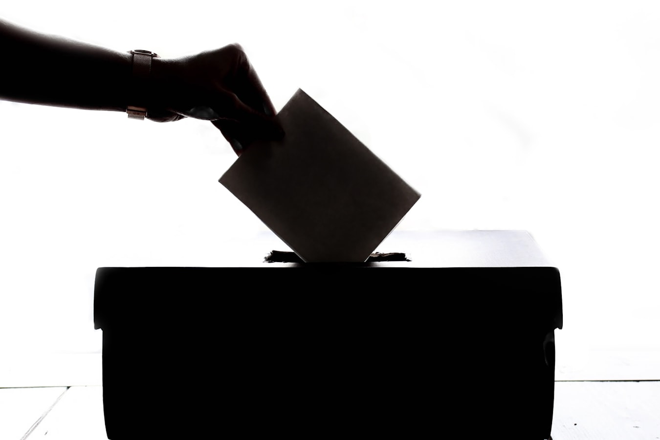 A hand putting a ballot in a box.