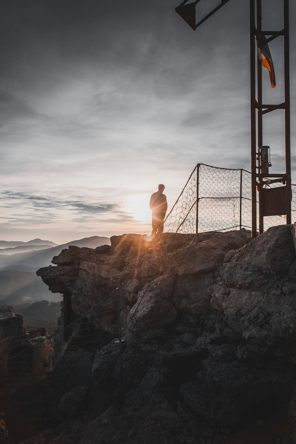 silhouette of man standing on cliff near metal fence