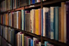 Rows of books neatly arranged on wooden shelves, showcasing various colors and sizes of book spines. The image captures a classic library setting with a close-up perspective focusing on the textures and titles of the books.
