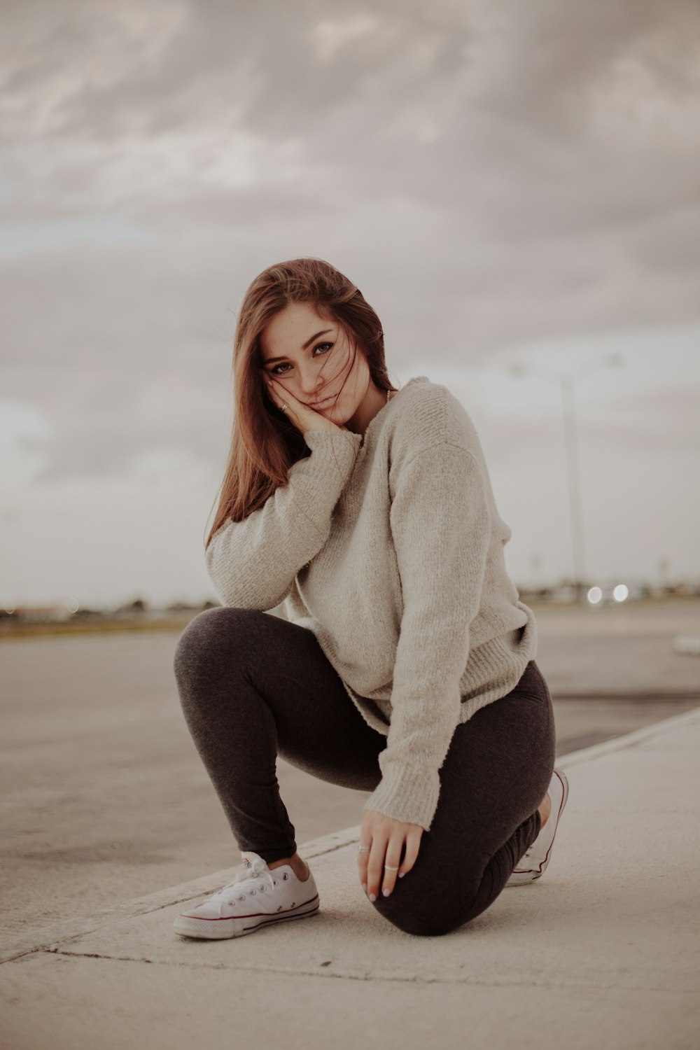 one unknown person kneeling on concrete road with hand on her cheek during daytime