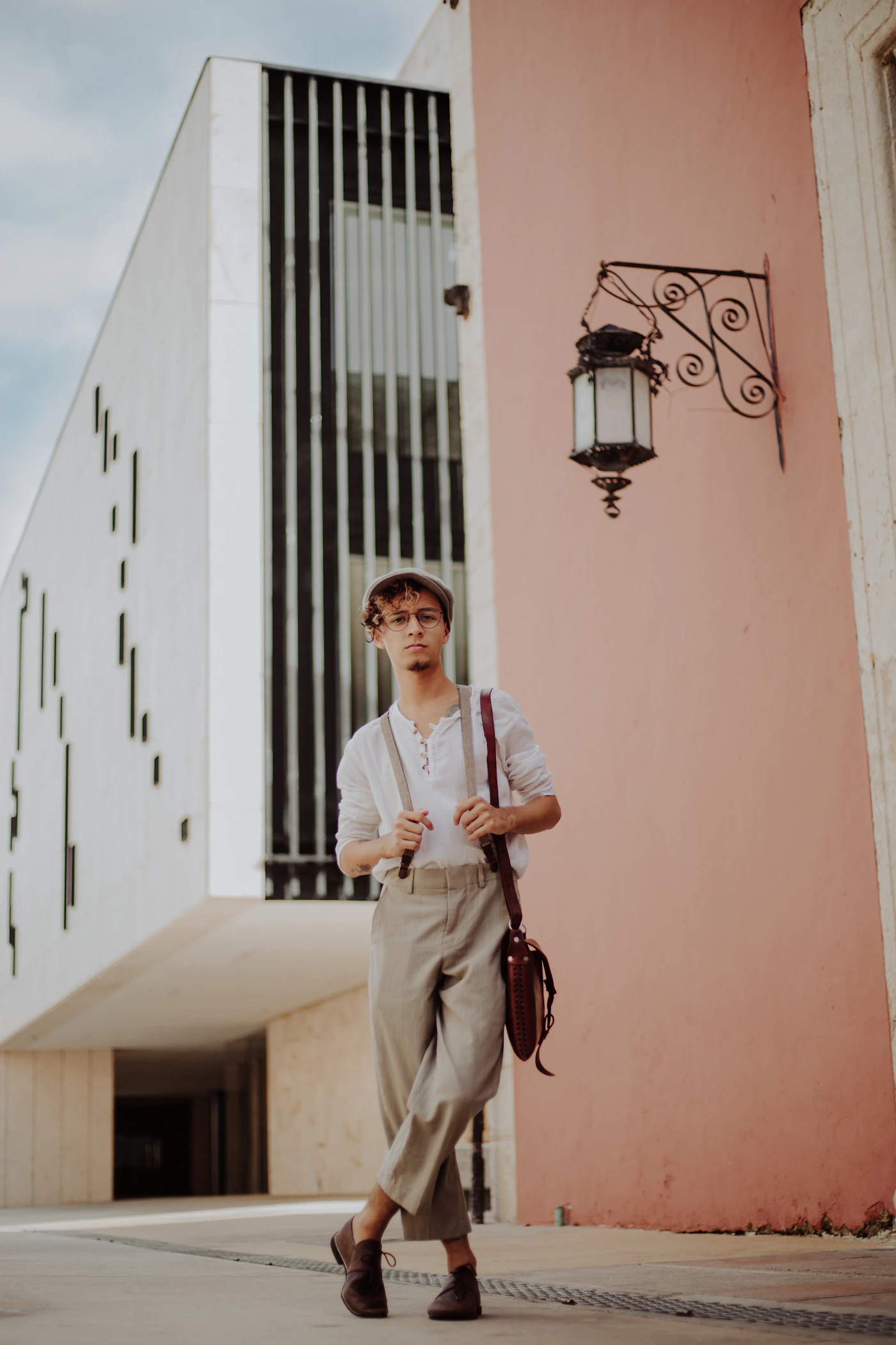 Man in stone pleated trousers and braces in front of a pink wall