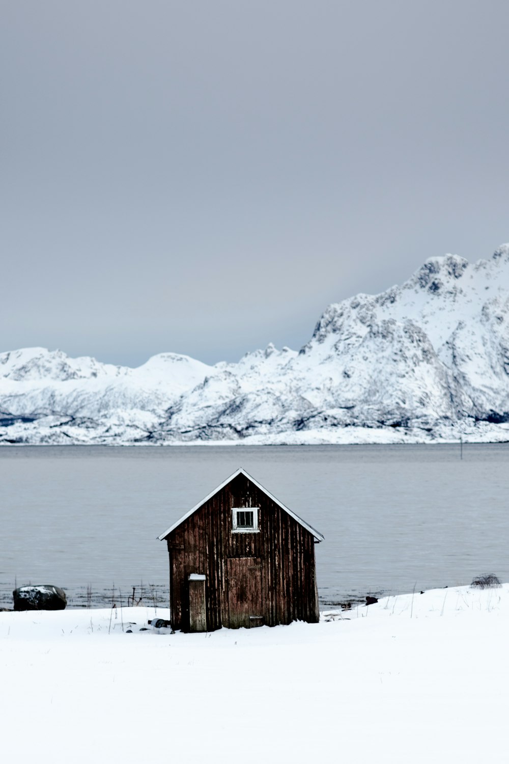 Brauner Holzschuppen in der Nähe eines Sees, umgeben von Schnee