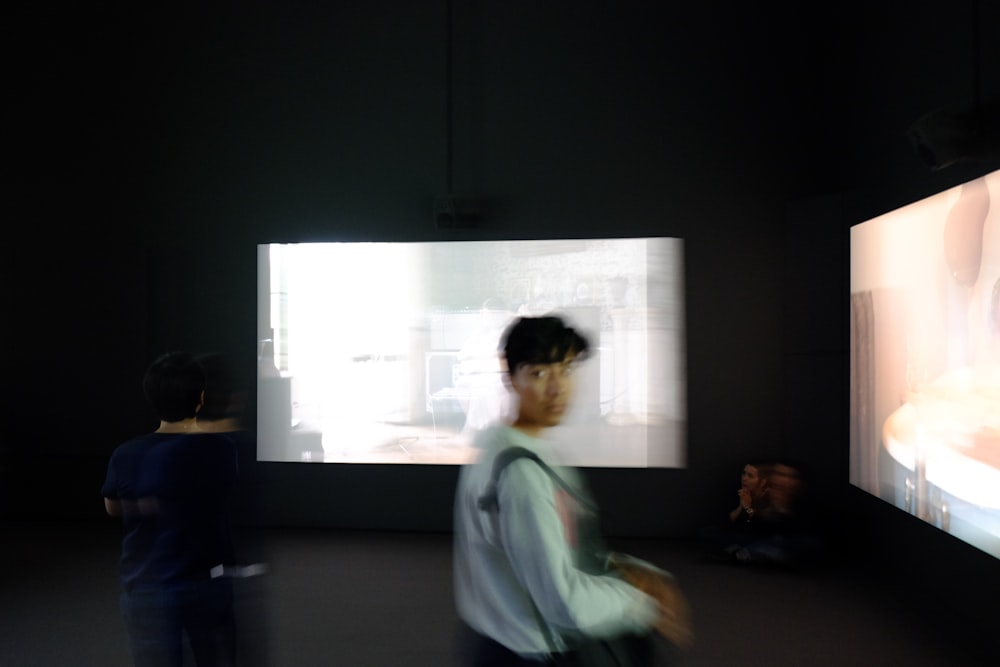 Persona in maglione grigio in piedi davanti a grandi monitor