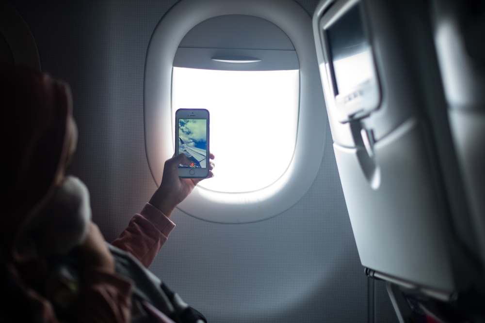 woman holding iPhone taking photo inside airplane