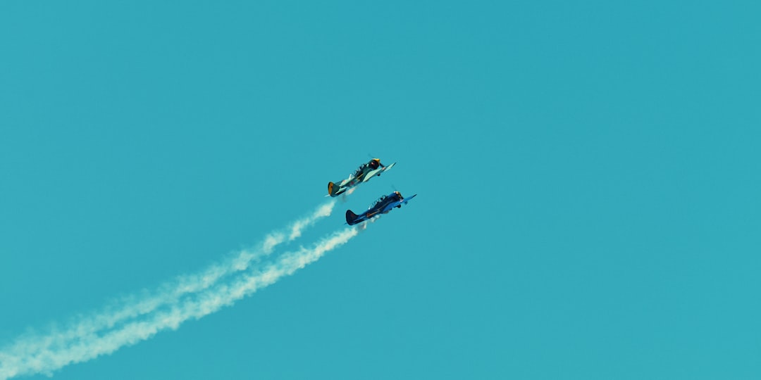 two blue planes in blue sky leaving white smoke trails