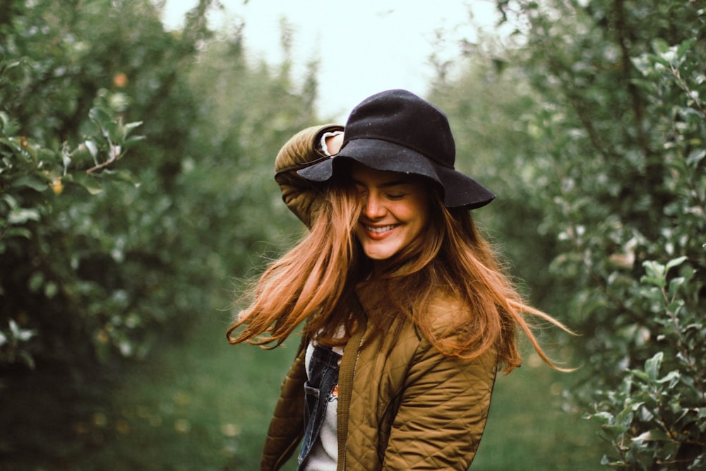 selective focus photography of woman holding her hat while smiling