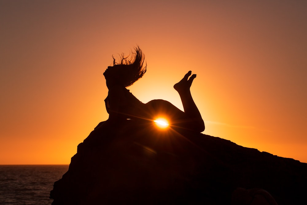 silhouette of woman with feet raised on air while lying with stomach on cliff edge