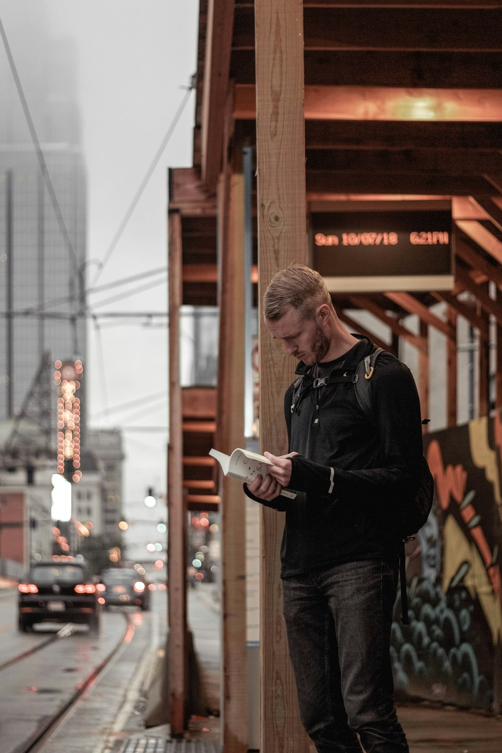man in black sweater stands on sidewalk with book in hand