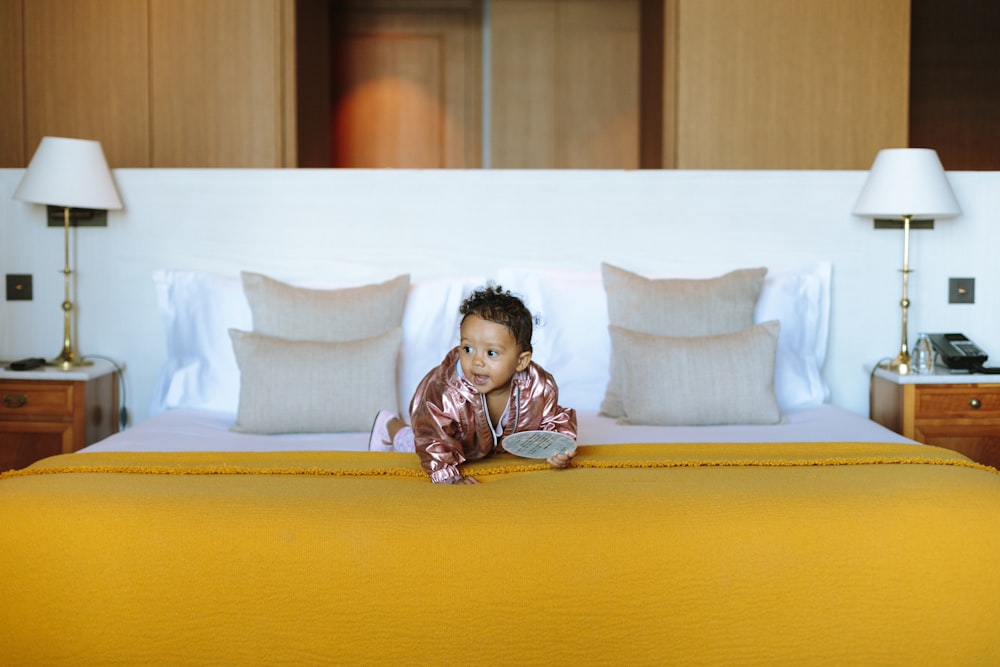 baby in pink jacket on yellow bed