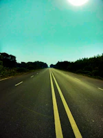 A freshly paved highway stretching under a clear blue sky with golden sunlight.