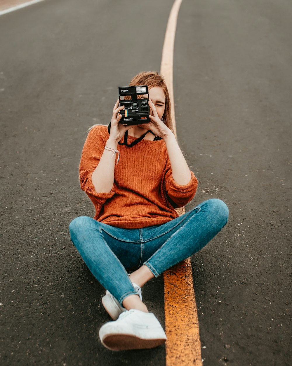 woman sitting at the middle of the road with one step camera during daytime