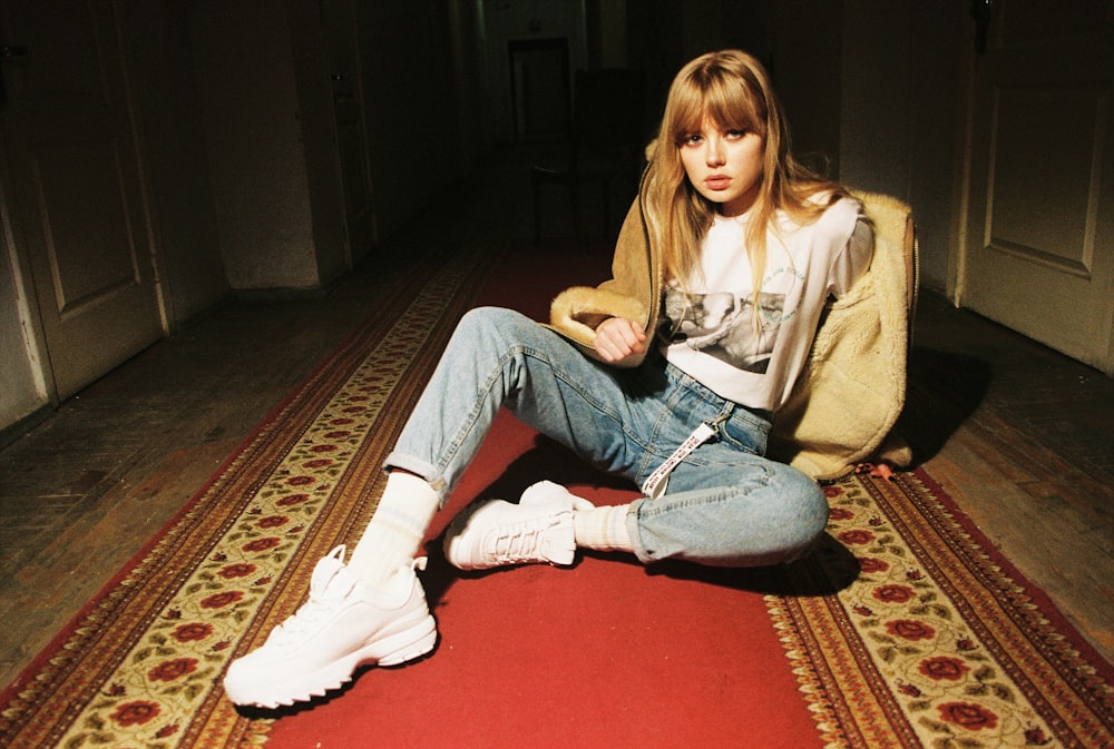 woman wearing brown jacket and blue denim jeans sitting on red carpet