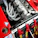 A detailed view of a high-performance car engine with multiple exhaust pipes and various mechanical components. Red safety harnesses are visible, hinting at a racing environment. The engine is housed in a red car with various decals and markings.