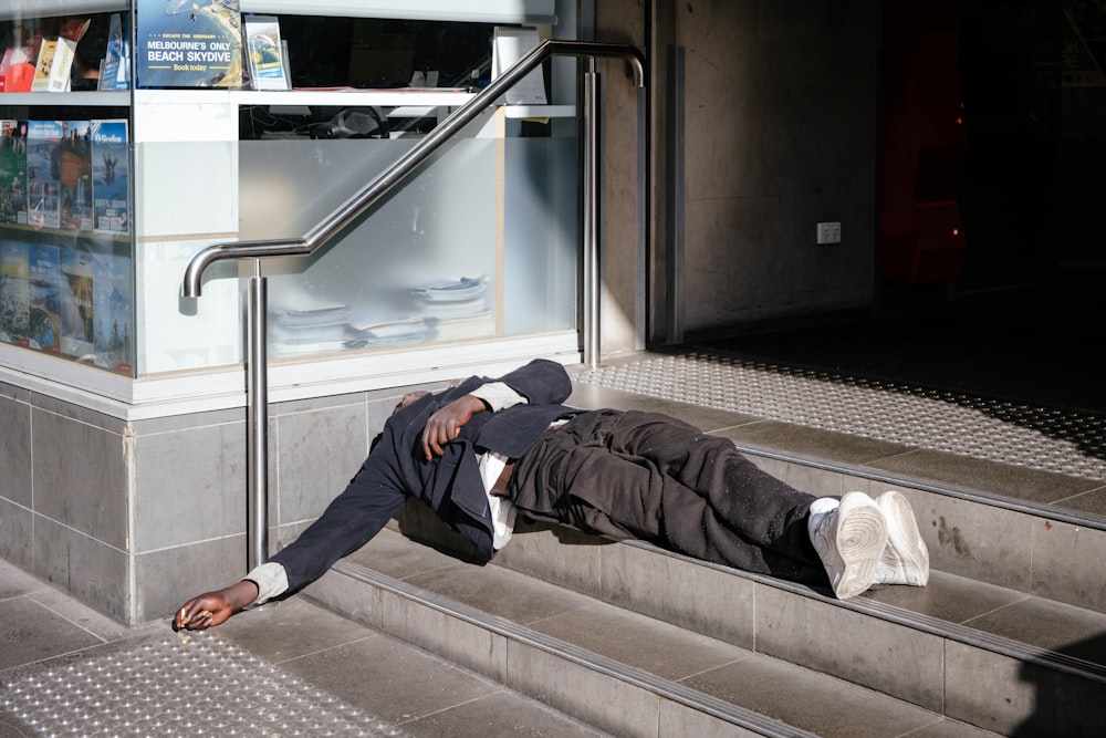 man wearing black blazer lying on gray stairs