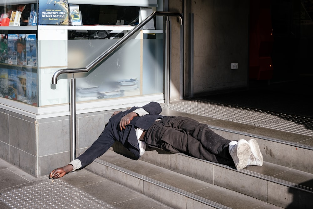 homem vestindo blazer preto deitado em escadas cinza