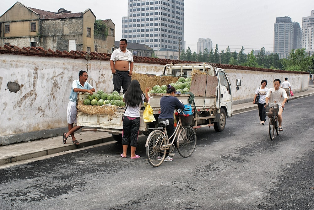 man standing on top of white pickup truck surrounded with green watermelon fruits