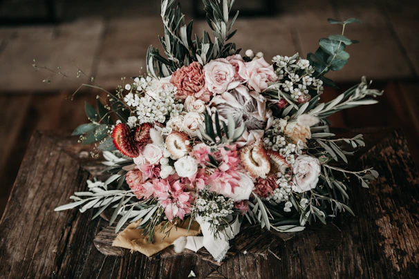 A vibrant bouquet of mixed seasonal flowers in soft pastel tones, artfully arranged on a rustic wooden table.